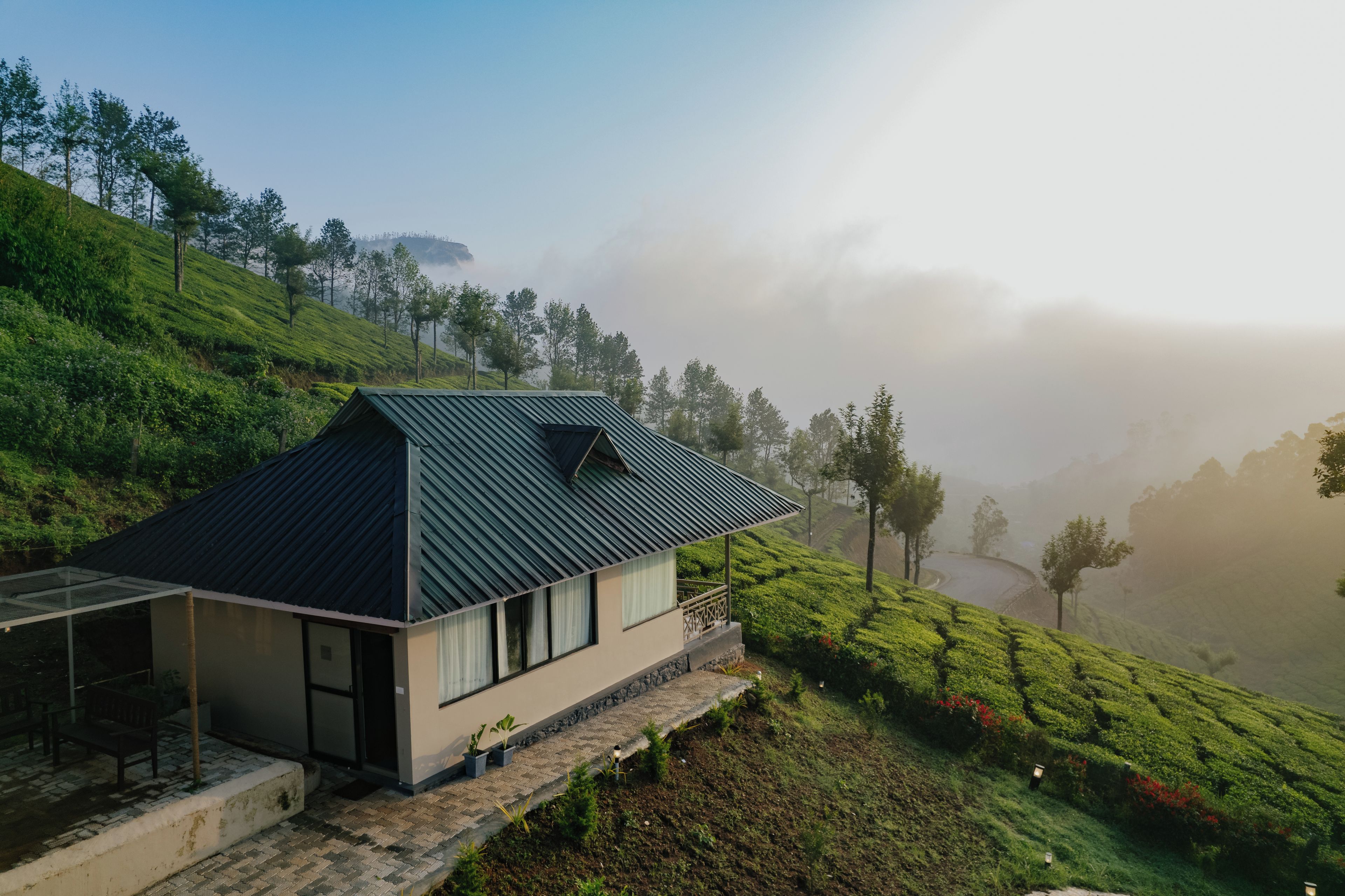 A modern house with a sloped roof, situated on a hillside with lush greenery and a misty background.
