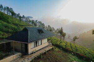 Una casa moderna con techo inclinado, ubicada en una ladera con abundante vegetación y un fondo brumoso.