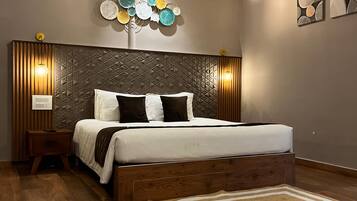Un dormitorio con cabecera de madera, cama con ropa de cama blanca, un adorno en la pared y suelo de madera.