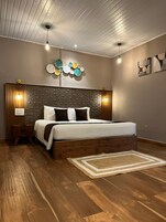 Un dormitorio con cabecera de madera, cama con ropa de cama blanca, un adorno en la pared y suelo de madera.