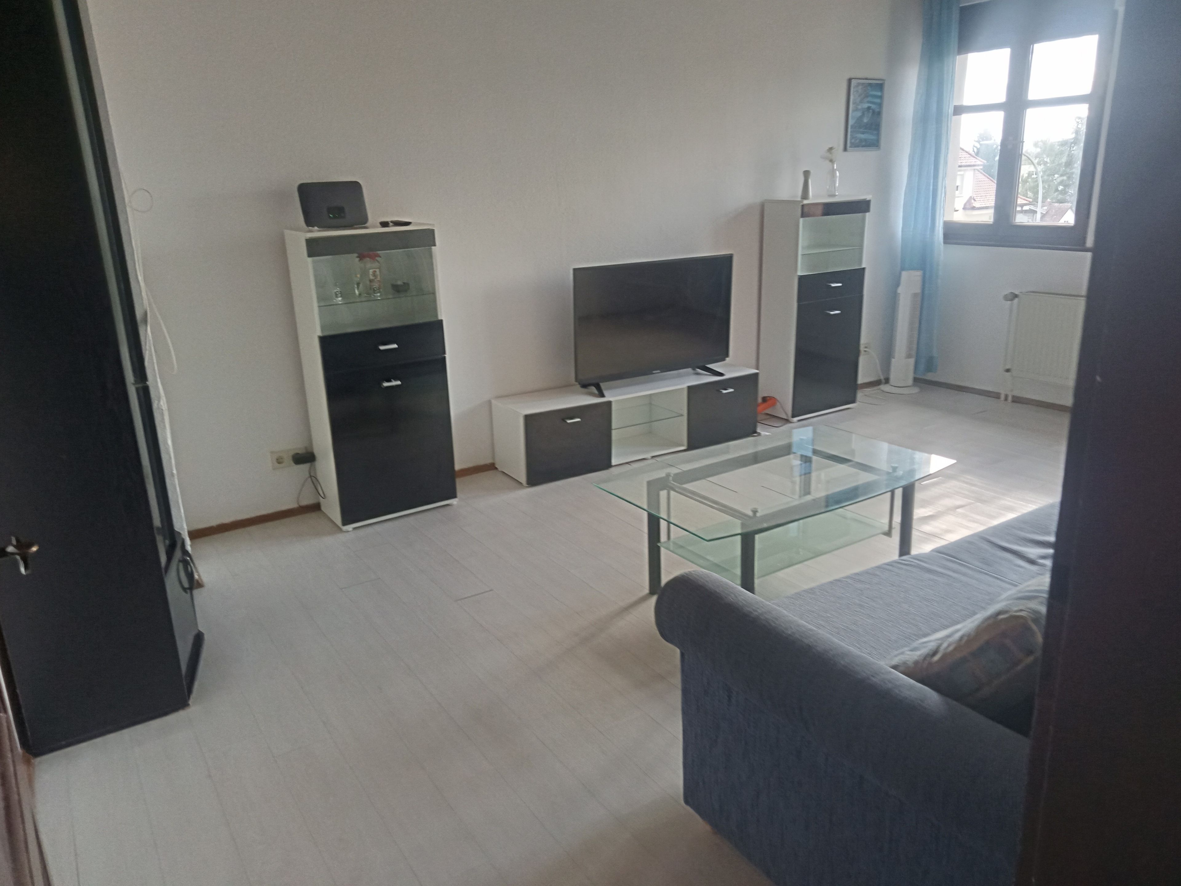 Ein Wohnzimmer mit einem Glastisch, einer Couch, einem Fernseher und integrierten Regalen.