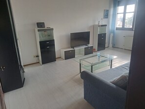 A living room with a glass coffee table, a sofa, a TV, and built-in shelving.