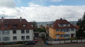 Una strada residenziale con case, cielo sereno e una vista lontana di un paesaggio urbano.