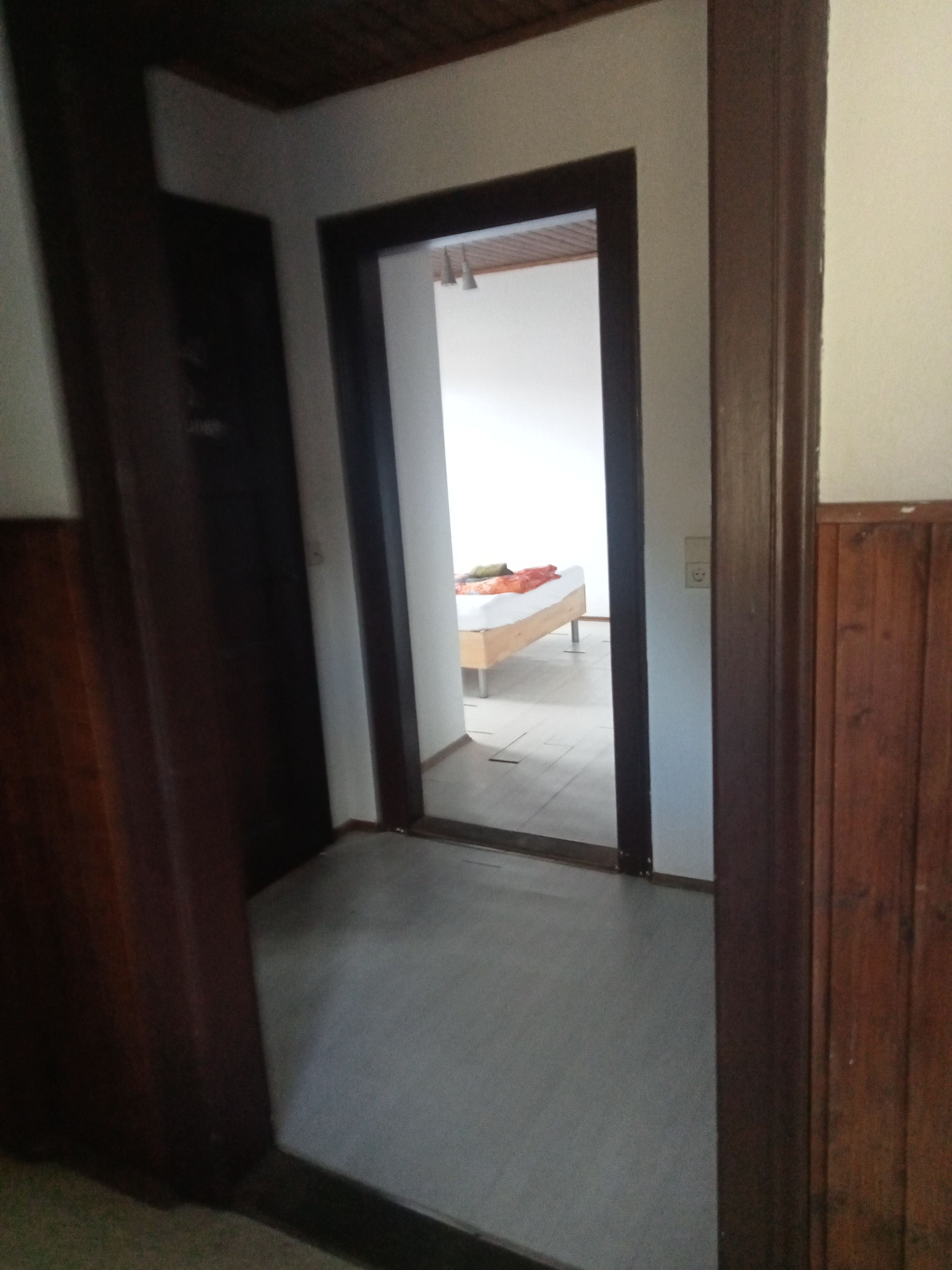Ein Flur mit einem hölzernen Türrahmen, der in ein Schlafzimmer mit einem Bett und einer weißen Wand führt.