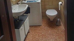 Un bagno piccolo con finestra, un lavandino, un water e una lavatrice.
