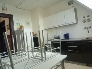 A kitchen with white cabinets, a microwave, a coffee maker, and a metal chair.