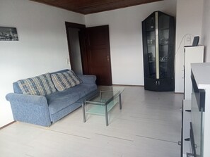Una sala de estar con un sofá, una mesa de centro de vidrio, un aparador y una puerta.