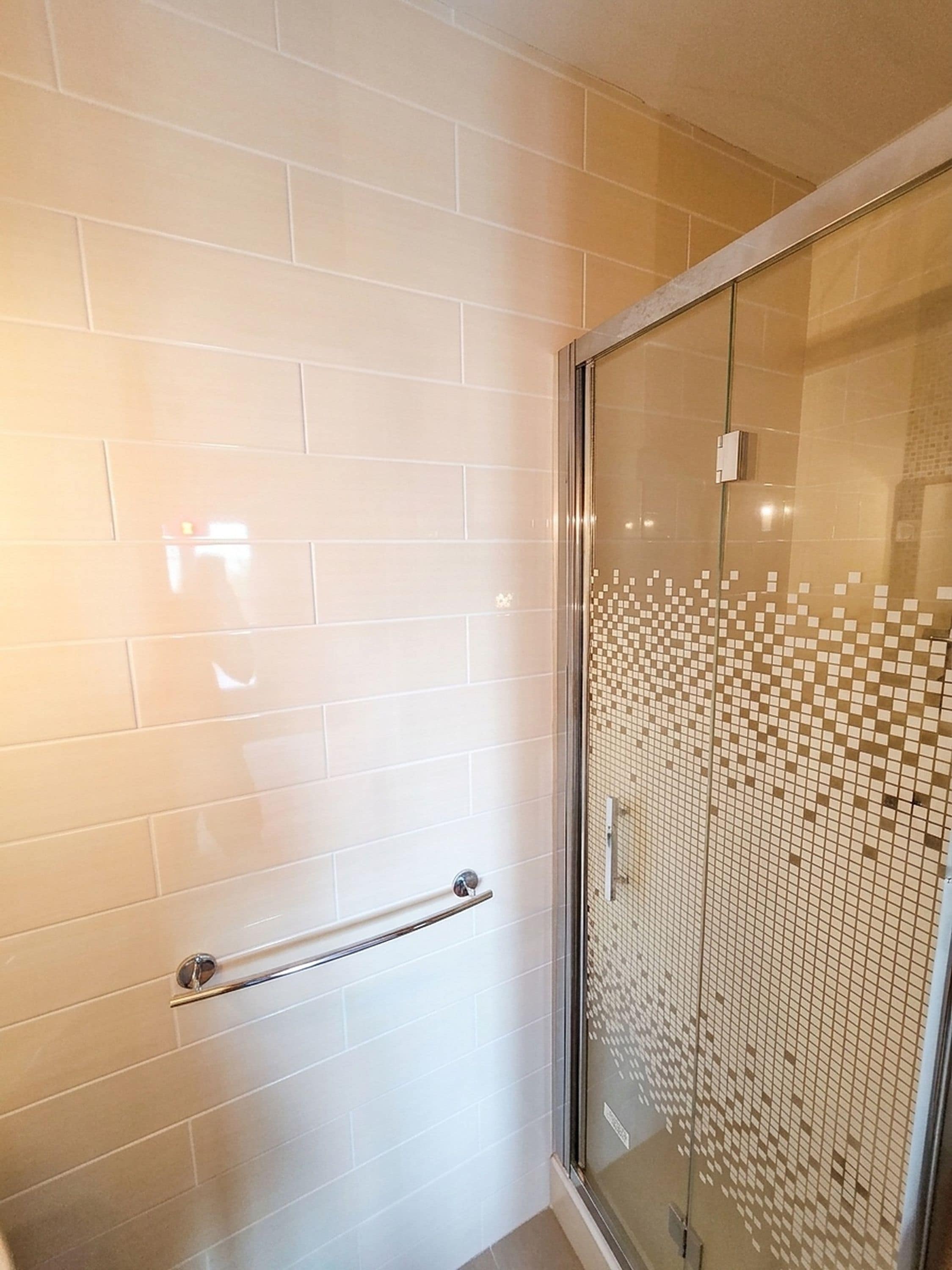 A bathroom with white tiled walls, a glass shower enclosure, and a handrail.
