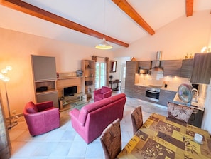 A modern living room with a sofa set, a dining table with chairs, a kitchen area with a microwave and stove, and a fireplace. - Villa Terrasse Olmeta-di-tuda Proche St Florent (Olmeta-di-Tuda)