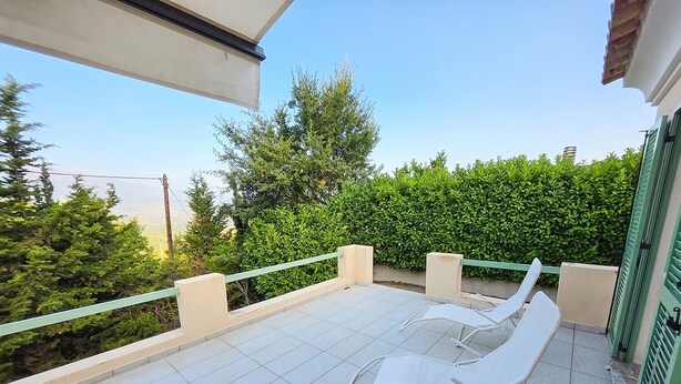 Ein Balkon mit zwei weißen Liegestühlen, gefliestem Boden und einem grünen Geländer.