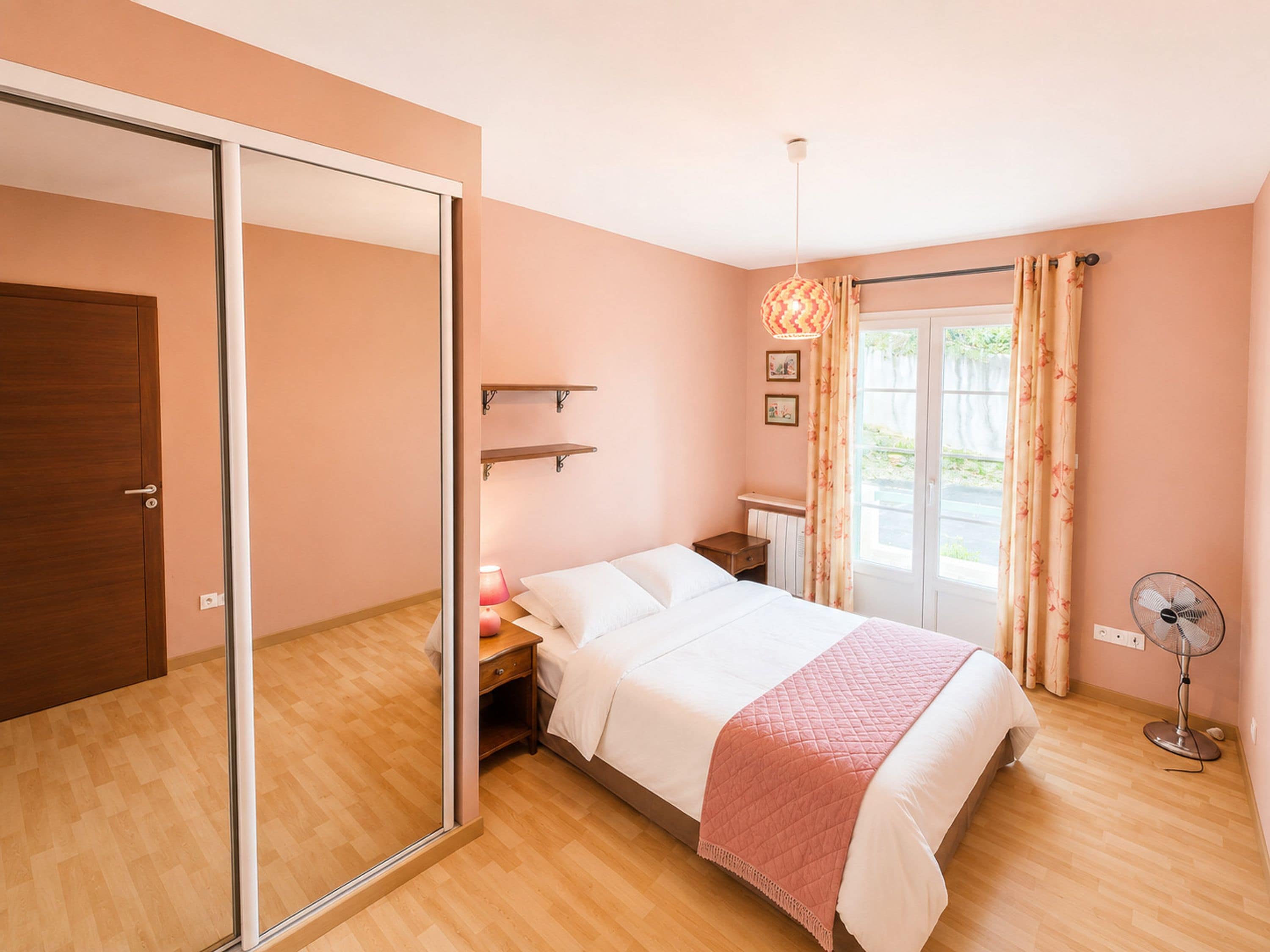A bedroom with a bed, bedside table, lamp, and a fan.
