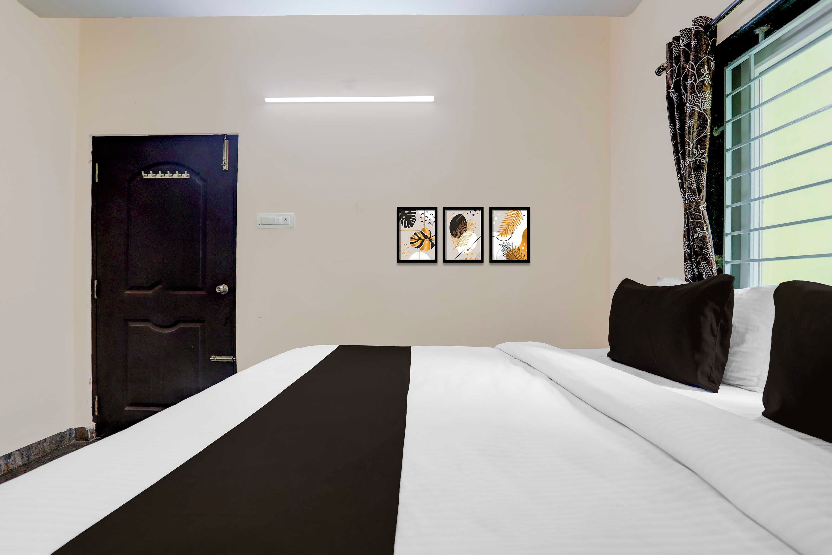 A hotel room with a bed, a door, and three framed pictures on the wall.