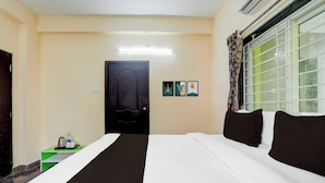 Una camera d'albergo con un letto, una porta, una finestra con tende e un tavolino con una bottiglia d'acqua e una tazza.