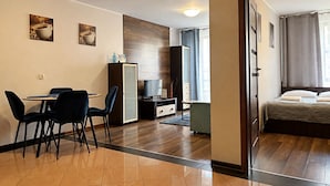 A hotel room with a bed, a desk with chairs, a television, and a wardrobe. - MARGI City 2B Apartament (Szczecin)