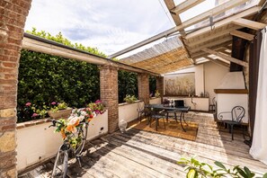 An outdoor patio with a wooden floor, a table with chairs, a bicycle, and potted plants. - Villa Querciolo - Surrounded by nature (Rosignano marittimo)