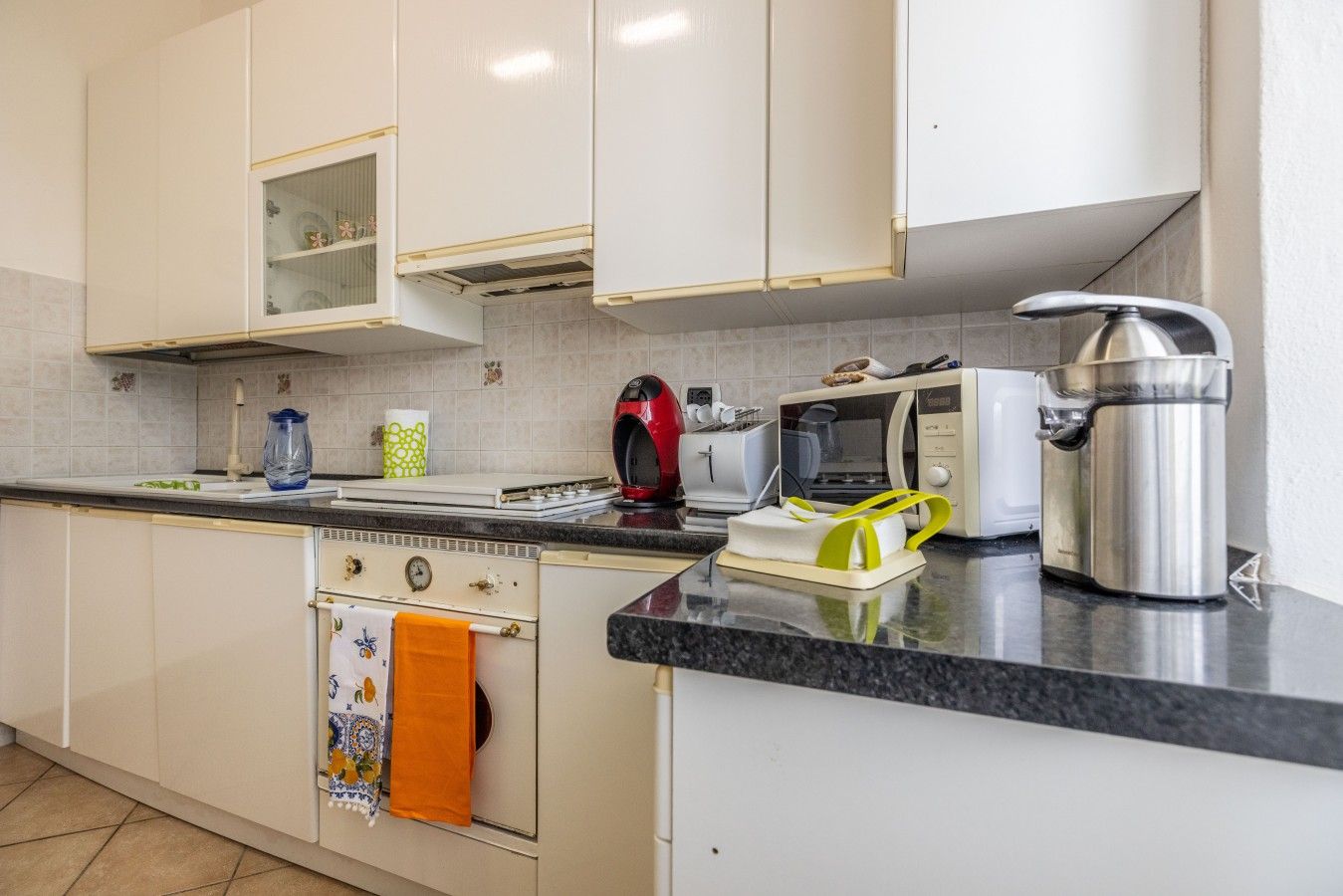 A kitchen with white cabinets, a stove, a microwave, a toaster, and a kettle.