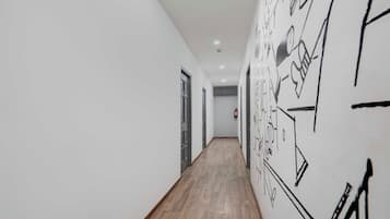 A hallway with a wooden floor, white walls, and black abstract wall art.