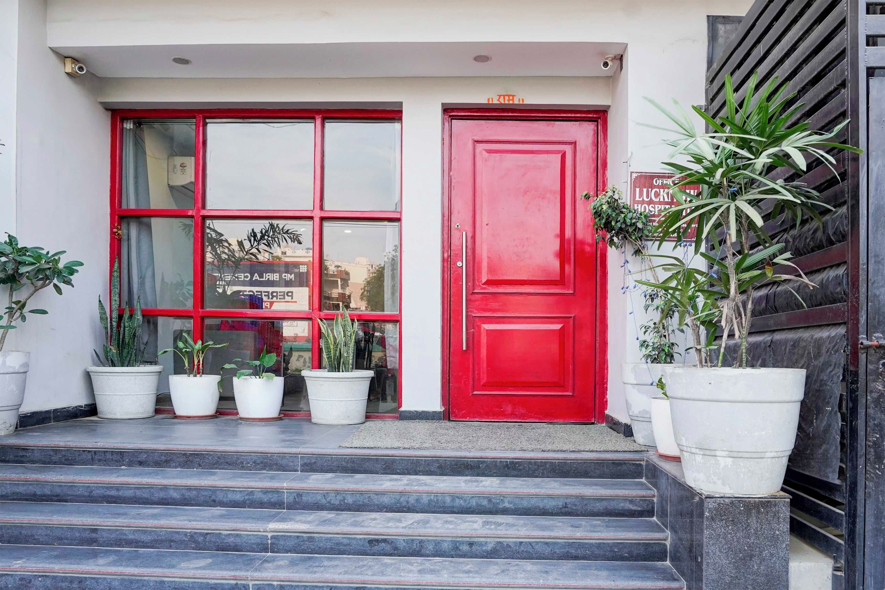 Entrada de un edificio con puerta roja, varias macetas y una escalera que sube.