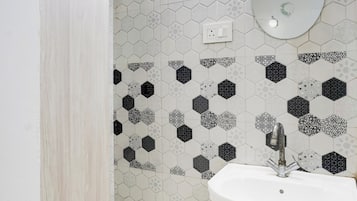 Un baño con un lavamanos blanco, un espejo y un revestimiento de pared con diseño hexagonal.