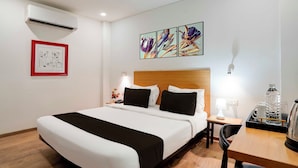 Una habitación de hotel con cama, mesita de noche, lámpara y un cuadro en la pared.