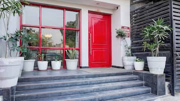A building entrance with a red door, multiple potted plants, and a staircase leading up to the entrance.