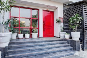 A building entrance with a red door, multiple potted plants, and a staircase leading up to the entrance. - Townhouse Oak Gomti Nagar Healthcity (Lucknow)