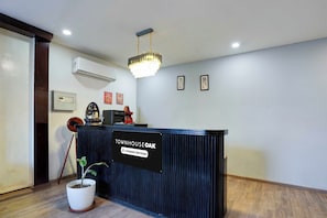 A reception desk with a sign indicating it is company-serviced, a potted plant, a ceiling light fixture, and framed artwork on the wall. - Townhouse Oak Gomti Nagar Healthcity (Lucknow)
