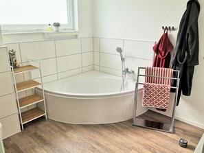 Ein Eckbadezimmer mit freistehender Badewanne, einem Metallregal und einem Handtuchhalter mit Handtüchern.