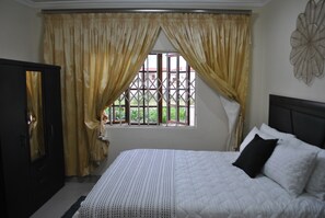 A bedroom with a bed, curtains, a window, and a wall decoration. - M and E Lodge (Polokwane)