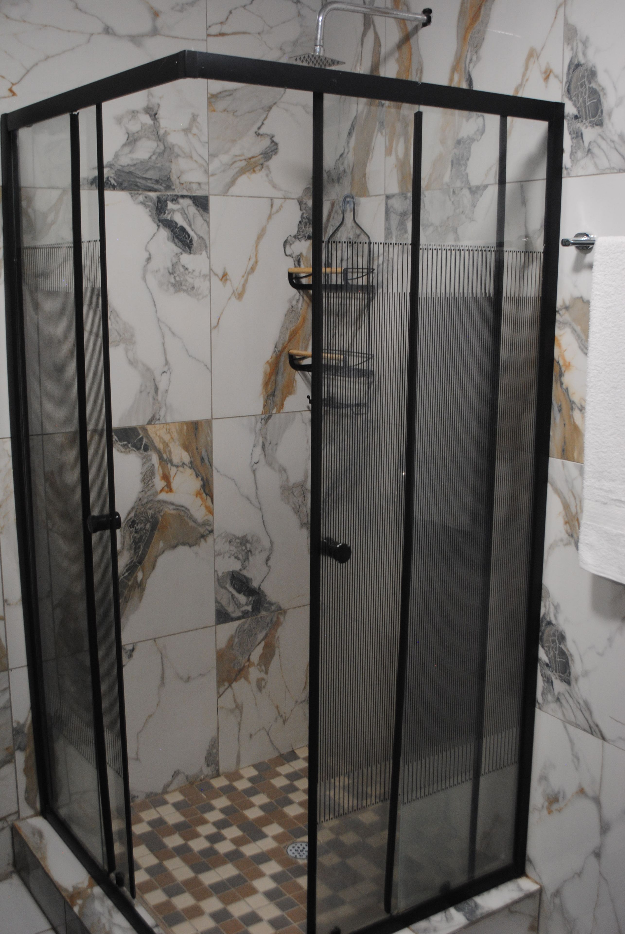 Un espace de douche d’angle avec un carrelage à motifs à carreaux et des murs en marbre.