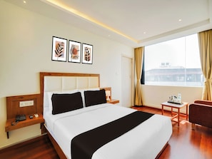 Une chambre d’hôtel avec un grand lit, une table de chevet, une chaise, une fenêtre avec des rideaux et des œuvres d’art accrochées au mur.