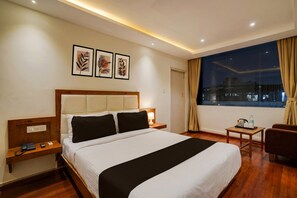 Une chambre d’hôtel avec un lit, une table de chevet, une lampe et une vue sur la ville la nuit.