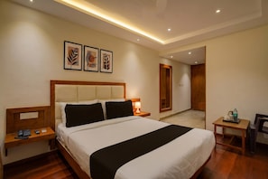 Une chambre d’hôtel avec un grand lit, des tables de chevet, un bureau et une chaise. Des tableaux encadrés ornent le mur, et une porte donne accès à une autre pièce.