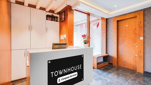 Un comptoir d’accueil avec une pancarte indiquant « TOWNHOUSE, services d’entreprise », situé dans un hall d’entrée moderne agrémenté d’éléments en bois et doté d’un sol en marbre.
