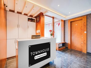 Un comptoir d’accueil avec une pancarte indiquant « TOWNHOUSE, services d’entreprise », situé dans un hall d’entrée moderne agrémenté d’éléments en bois et doté d’un sol en marbre.