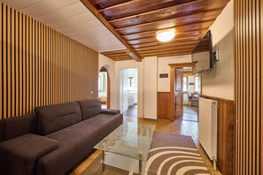 Ein modernes Interieur mit einer Couch, einem Glastisch, Holzvertäfelung und einer Decke mit freiliegenden Balken.