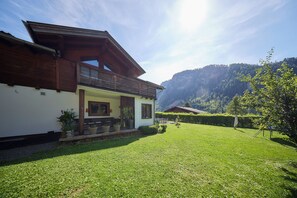 Ein zweigeschossiges Haus mit einem Balkon, einem gepflegten Rasen und einer Bergkulisse im Hintergrund.