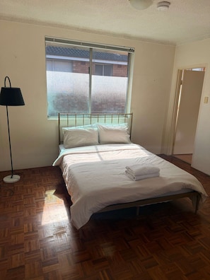 Een slaapkamer met een bed, een raam, een vloerlamp en een deur.