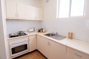 A kitchen with white cabinets, a stove, an oven, a sink, and a window. - Bondi Studio | 2 Min Walk to Beach, Queen Bed, Separate Kitchen (Bondi Beach)