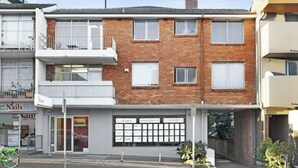 Un edificio residencial de dos pisos con fachada de ladrillo, un balcón en el nivel superior y entrada a un garaje.