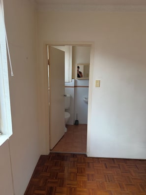 Een gang die uitkomt bij een badkamer met toilet, een hygiëneschuimer en een spiegel.