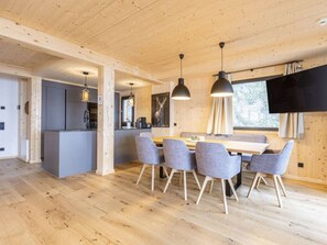 Ein modernes Interieur mit Holzboden, einem Essbereich mit grau gepolsterten Stühlen und einer Küche mit grauen Schränken.