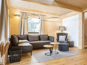 A cozy living area with a sofa, armchair, and small coffee table, wooden flooring, and a window with curtains. - Superior Chalet #13 With Sauna & Hot Tub (Stadl-Predlitz)