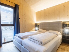 Ein Zimmer mit einem Bett, Holzwänden, einem Fenster mit Vorhängen und einem Nachttisch mit einer Lampe.