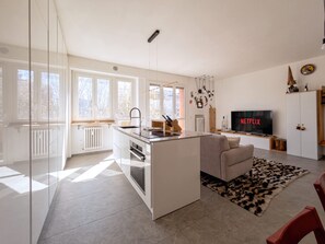 Eine moderne Küche mit einer zentralen Kochinsel, einem Essbereich mit einer Couch, einem Flachbildfernseher und einem großen Fenster.