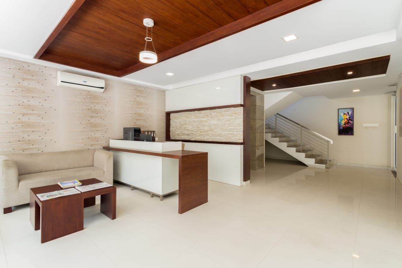 A modern reception area with a reception desk, a sofa, and a coffee table. There is a staircase leading to another level.