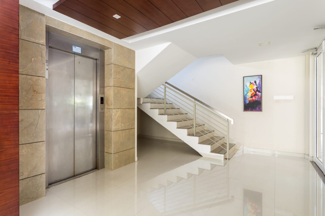 Un ascensor moderno, una escalera y una pared con una obra de arte enmarcada.