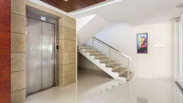 Un ascensor moderno, una escalera y una pared con una obra de arte enmarcada.
