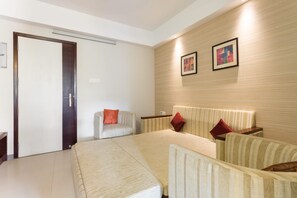 A hotel room with a bed, a sofa, a chair, a bedside table, and a wall-mounted artwork. - D Homz Suites (Ernakulam)