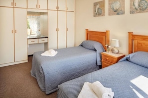 A hotel room with two beds, a wooden headboard, a nightstand with a lamp, and artwork on the wall.